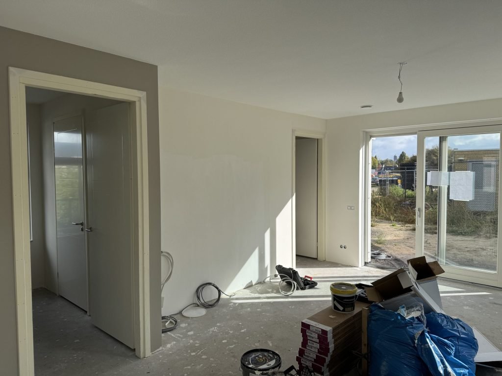 Woonkamer tijdens de afwerking met deuren naar andere ruimtes en materiaal op de vloer