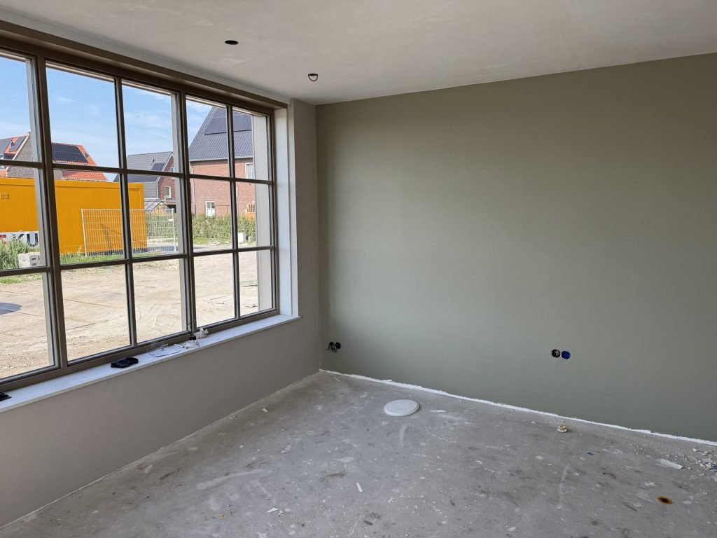 Kamer met een wand in een grijsgroene tint naast een breed raam met veel daglicht