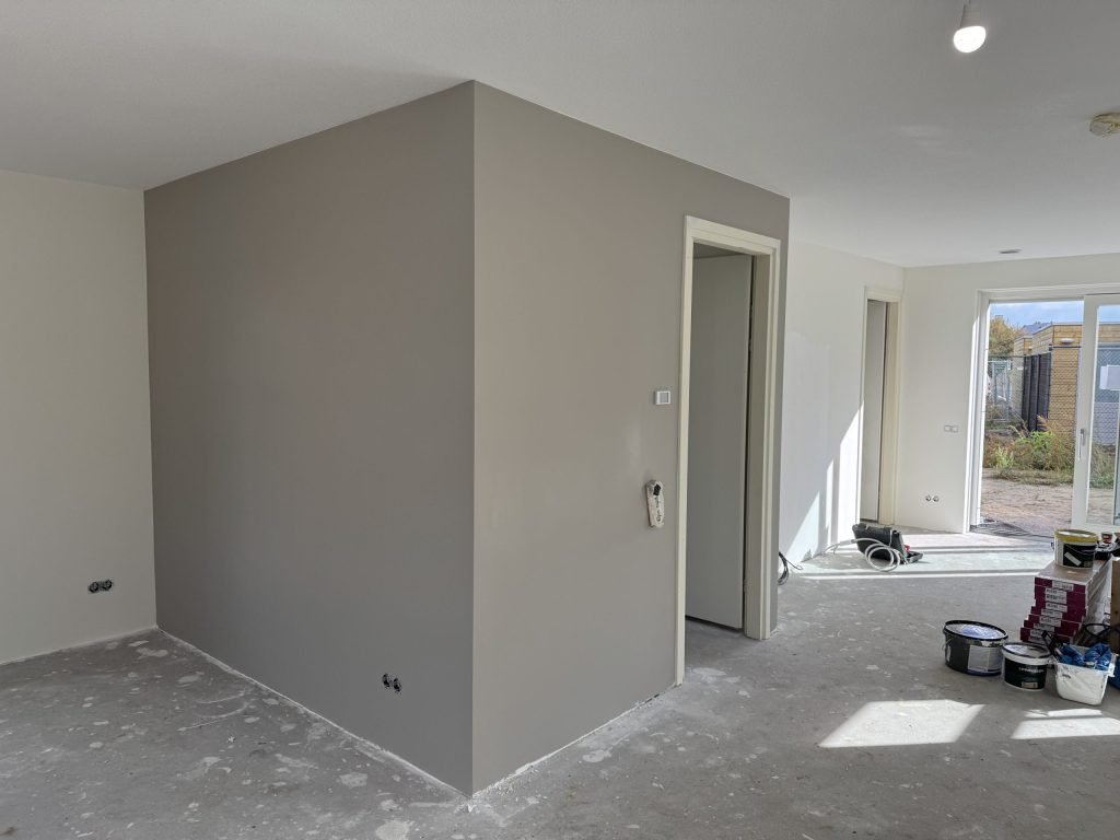 Grijze wand met een uitstekende hoek en een deuropening in een woning tijdens de afwerking