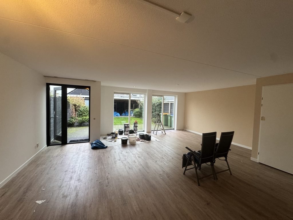Ruime woonkamer met lichte gesausde wanden, een houten vloer en tuindeuren